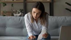 Young woman going over 金融s on couch at home with calculator, laptop, and receipts.